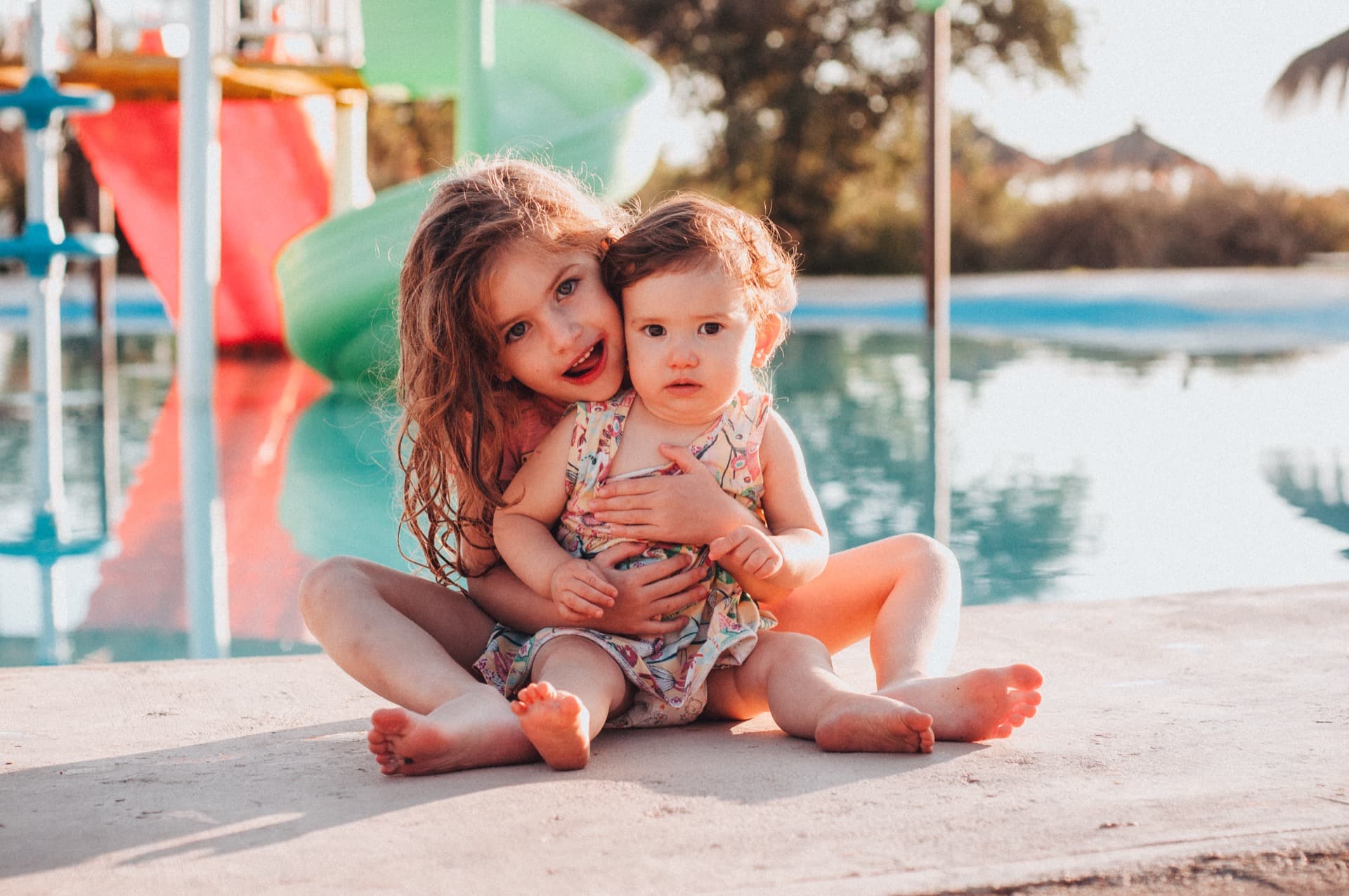 Two young sisters hugging at the poolside in summer light