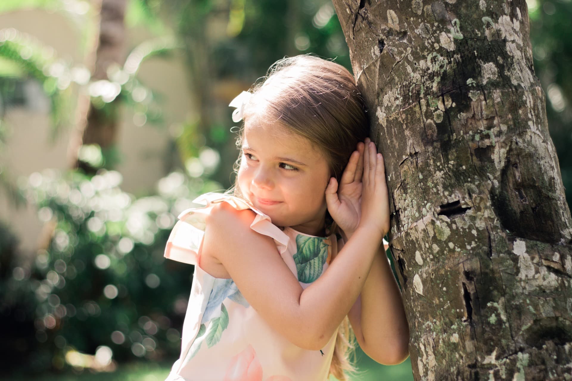 Young girl leaning against a tree, daydreaming in dappled sunlight
